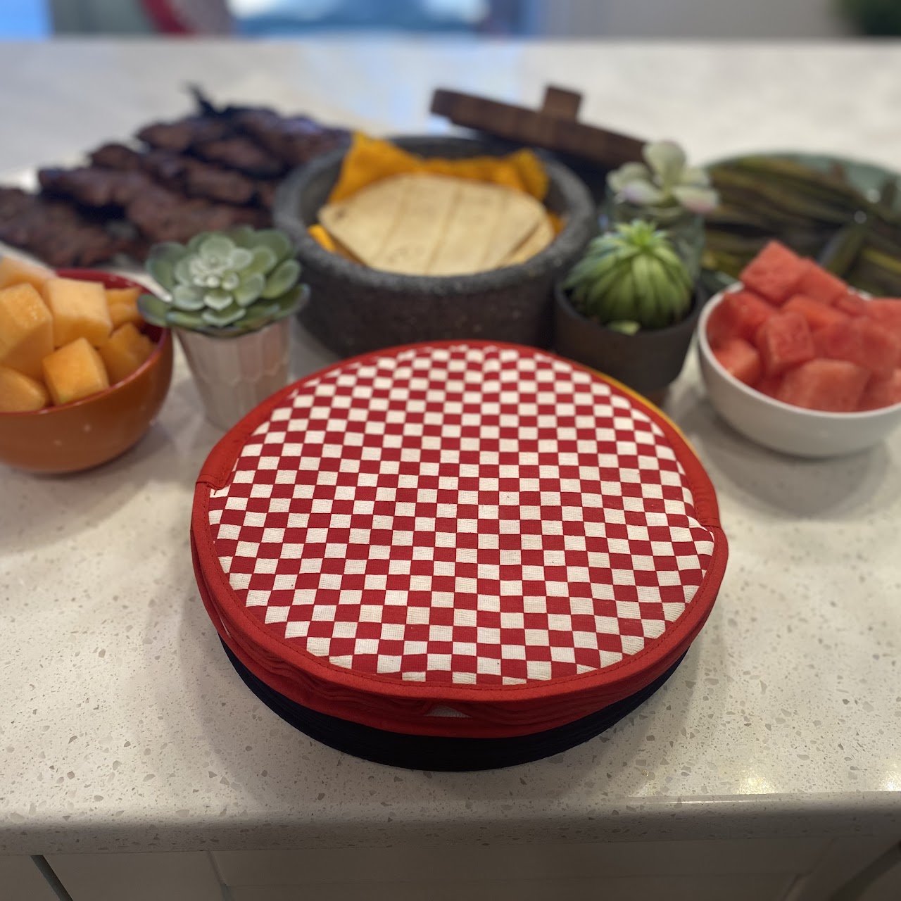 Red gingham Ezee Heat tortilla warmer on a table with tortillas and fresh food